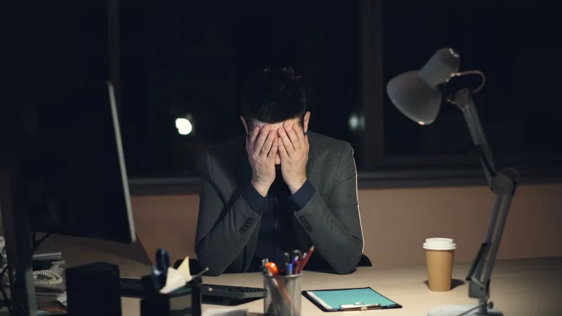 A man at his desk late at night with his head in his hands