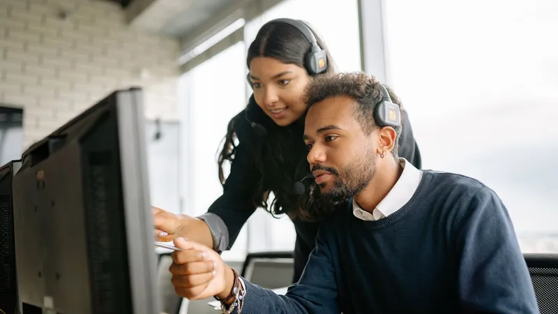 Two support colleagues wearing headsets working through an issue on a monitor together