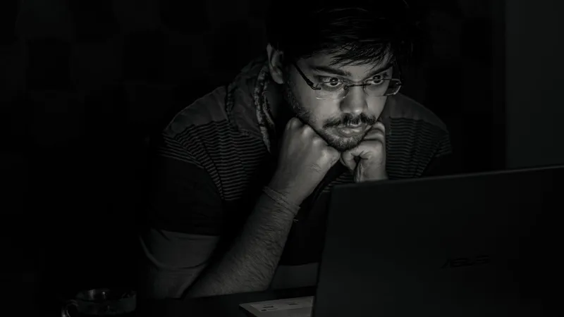 A developer staring intently at a laptop screen in a dark room late at night